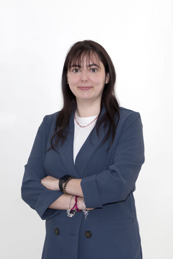 Mujer mediana edad con cabello negro largo Tiene ojos verdes oscuros. En la foto aparece con los brazos cruzados sonriendo